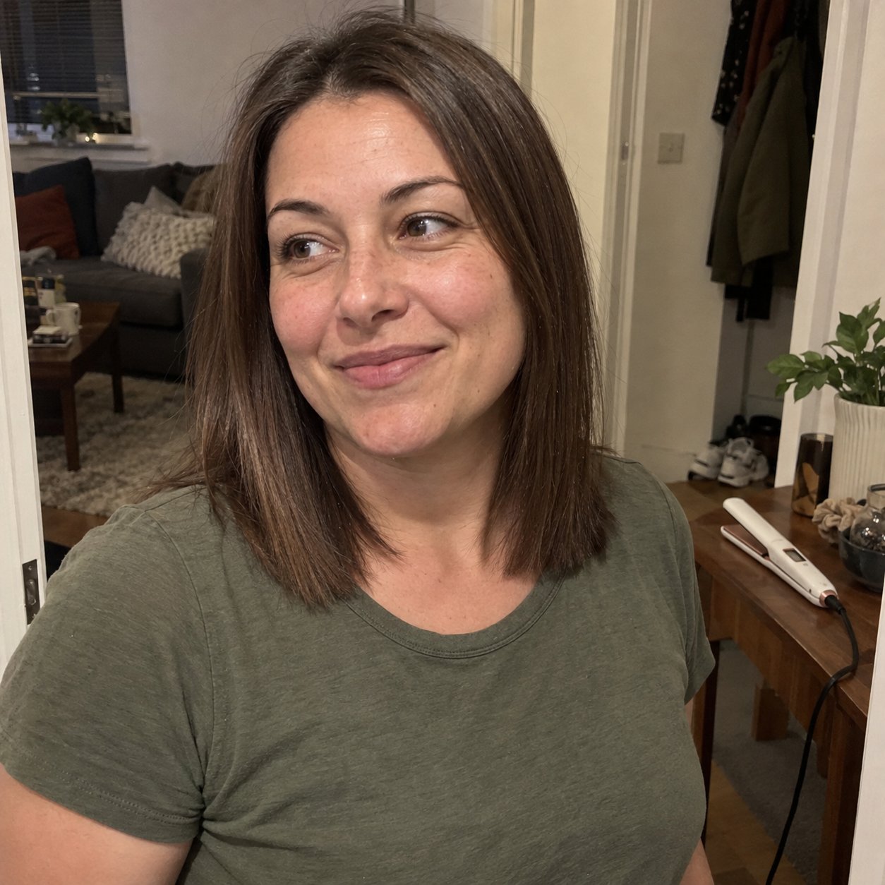 Real customer photo: woman with sleek shoulder-length straight brown hair at home, the white SalonGlide resting on a table behind her