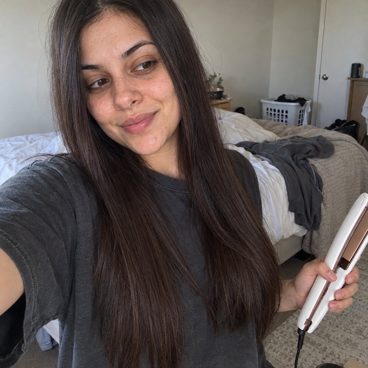Real customer photo: woman with long sleek straight dark hair taking a selfie while holding the white SalonGlide in her bedroom